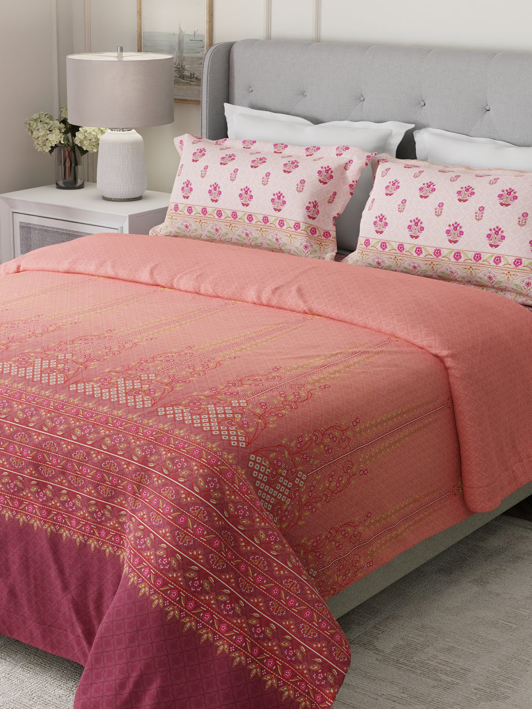 Bed with pink and purple patterned bedding and floral pillows in a bedroom setting.
