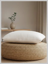 White pillow on a woven ottoman with a neutral background