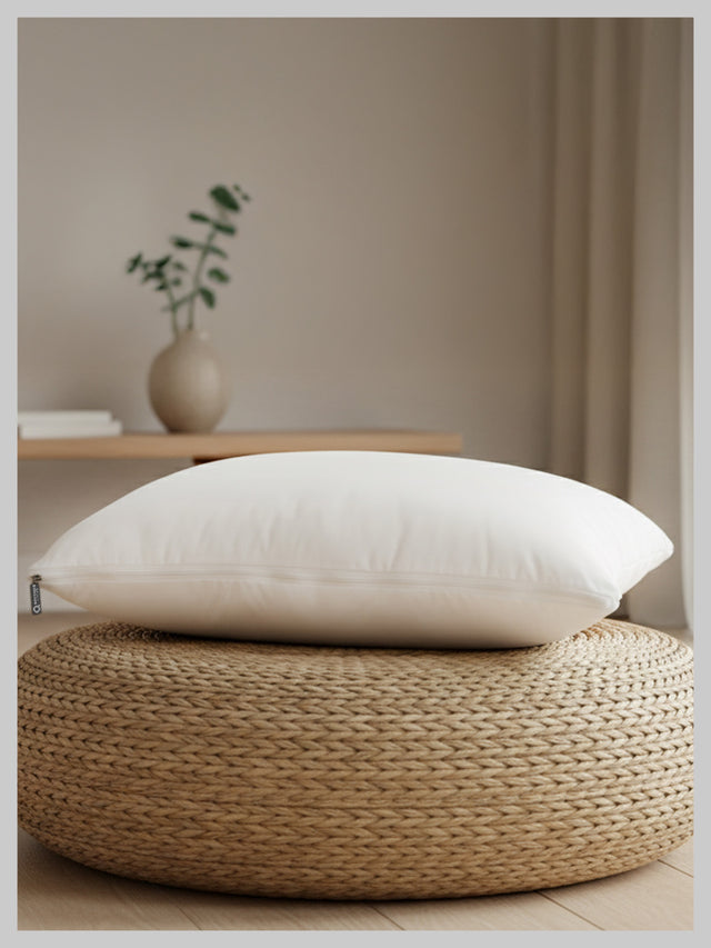 White pillow on a woven ottoman with a neutral background